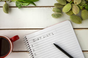 Flat lay of wooden white tray red coffee cup unripe almonds white notebook diet list written on white sheet