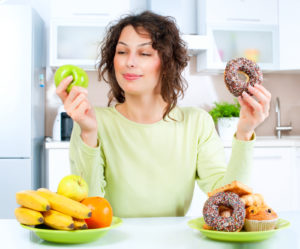 Diet. Dieting concept. Healthy Food. Beautiful Young Woman choosing between Fruits and Sweets. Weight Loss